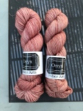 Onyx Fiber Arts Worsted in Sophia. a soft pink, on a glass table reflecting a vine-covered pergola